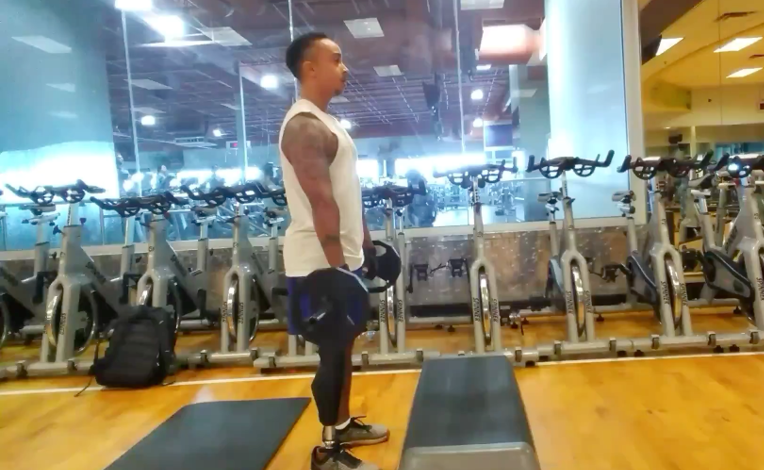 Man with prosthesis holding weights in a gym in front of a mat and stationary cycles